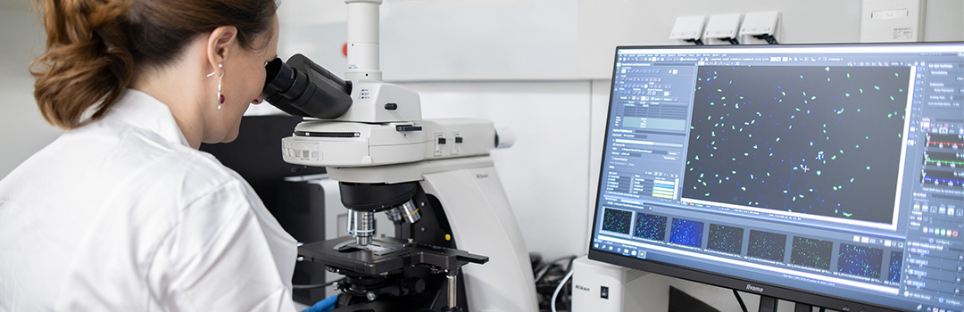 Frau im Laborkittel sieht durch Mikroskop